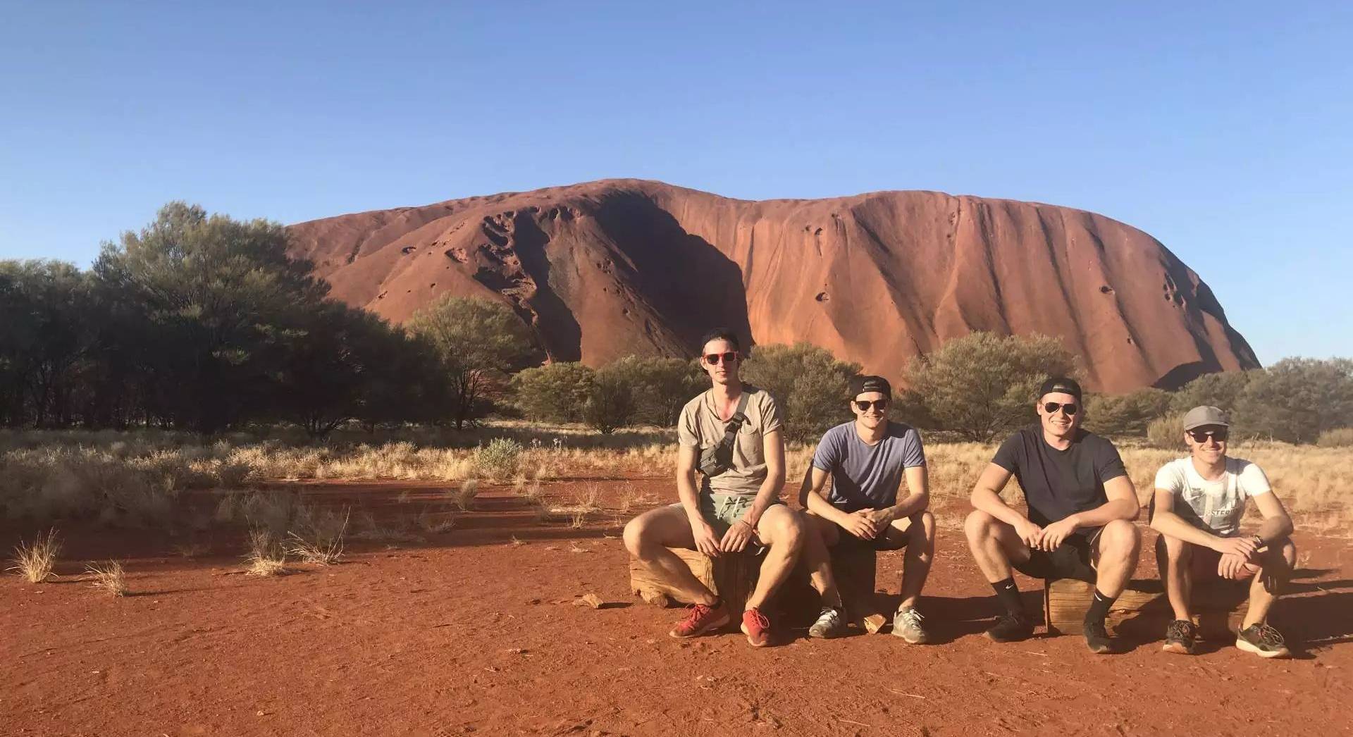 Studierende sitzend vor dem Ayers Rock in Australien