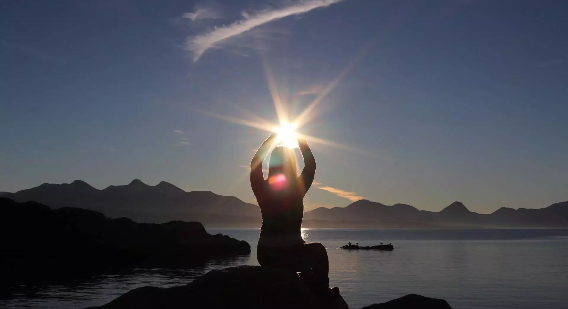 Student sits on a rocky outcrop and reaches out for the sun