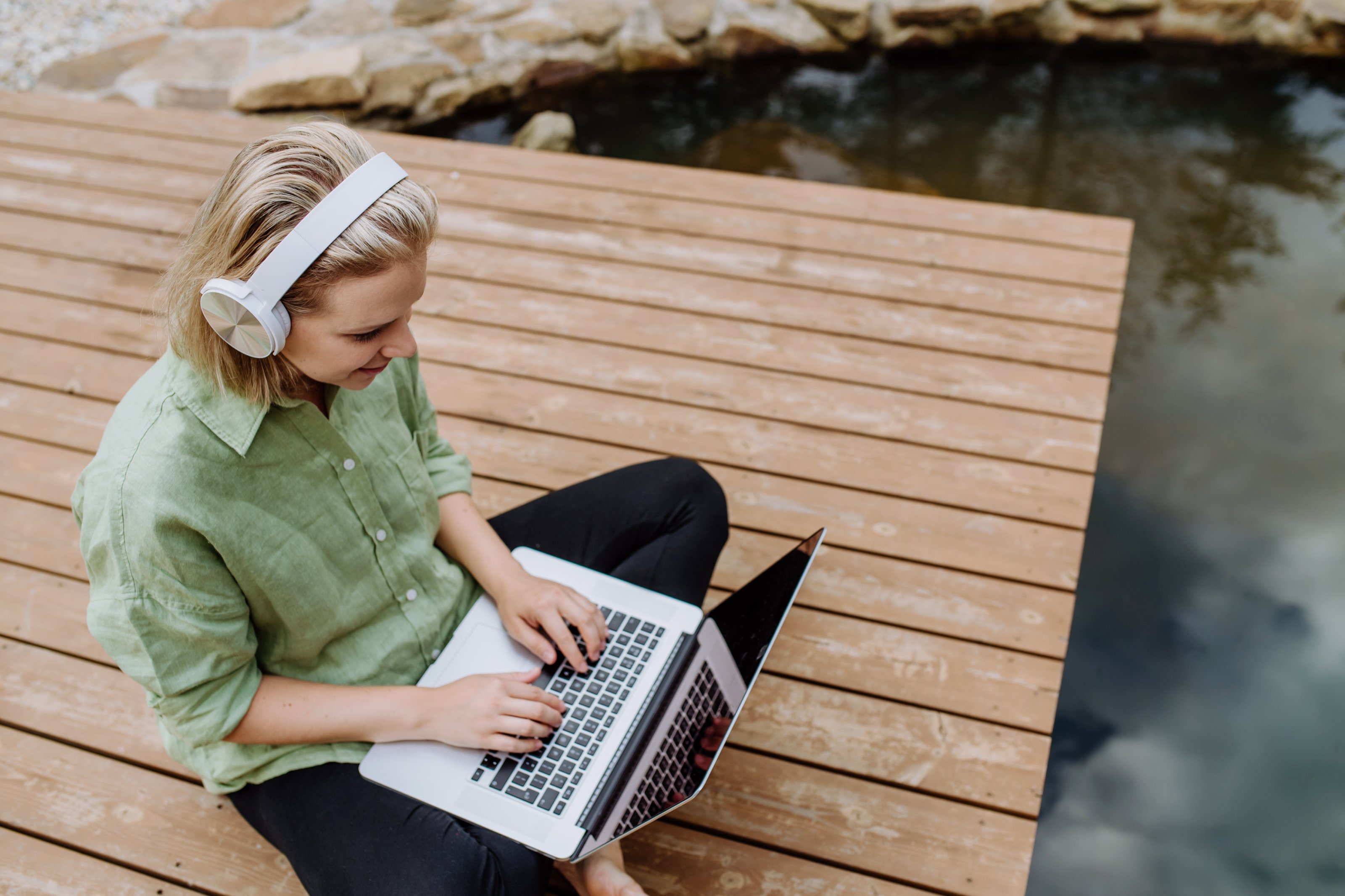 Junge Frau mit Laptop und Kopfhörern am See Junge Frau mit Laptop und Kopfhörern am See
