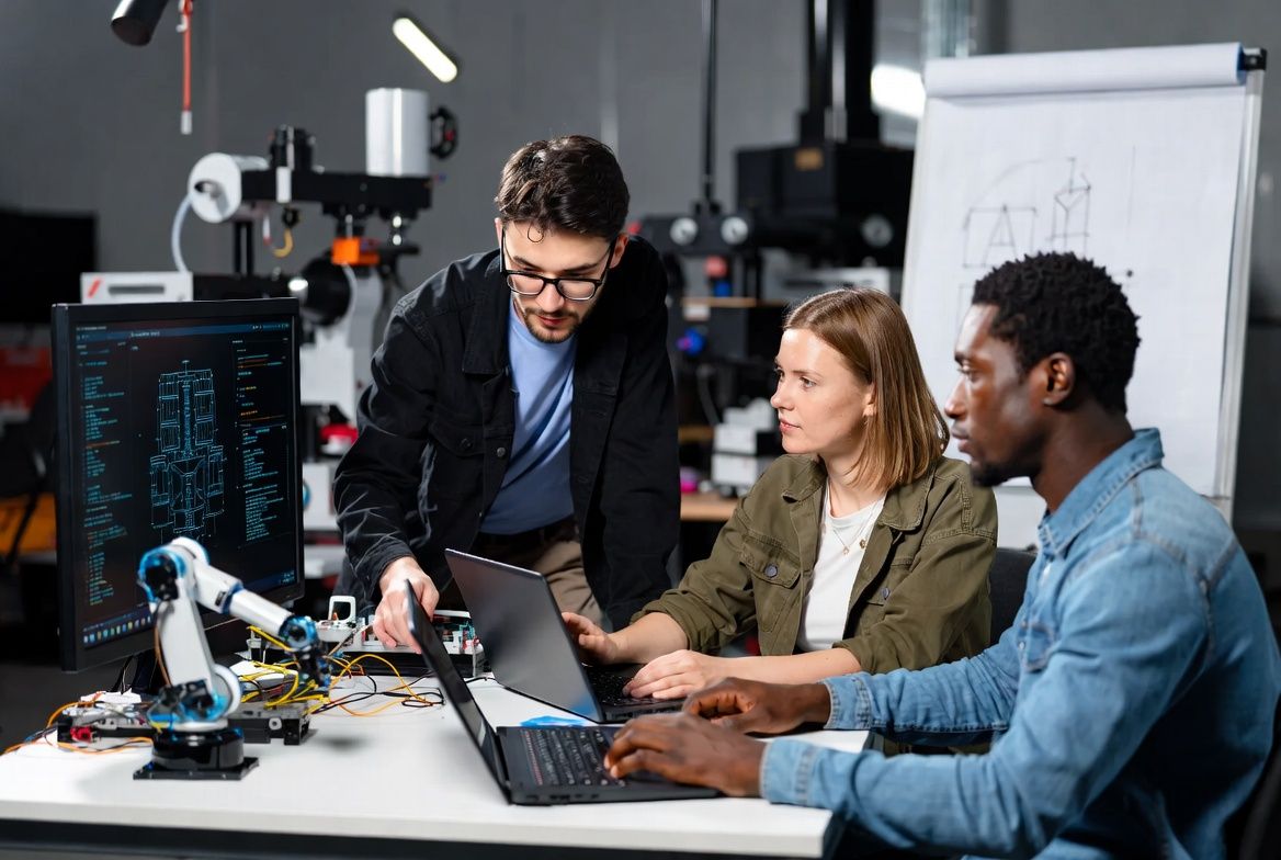 Ein interdisziplinäres Team arbeitet in einem Labor an der Entwicklung digitaler Technologien. Zu sehen sind Computer, Programmierumgebung und ein Roboterarm als Beispiele für moderne Automatisierungs- und KI-Anwendungen. Ein interdisziplinäres Team arbeitet in einem Labor an der Entwicklung digitaler Technologien. Zu sehen sind Computer, Programmierumgebung und ein Roboterarm als Beispiele für moderne Automatisierungs- und KI-Anwendungen.