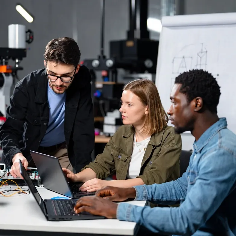 Ein Team arbeitet in einem Labor an der Entwicklung digitaler Technologien. Zu sehen sind Computer, Programmierumgebung und ein Roboterarm als Beispiele für moderne Automatisierungs- und KI-Anwendungen.