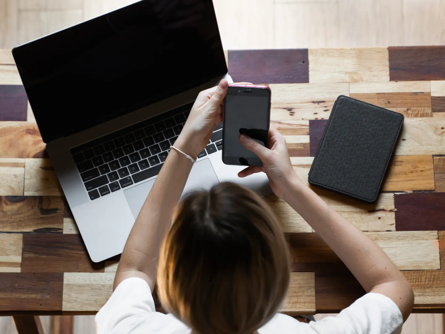 A person is working on a cell phone and a laptop.