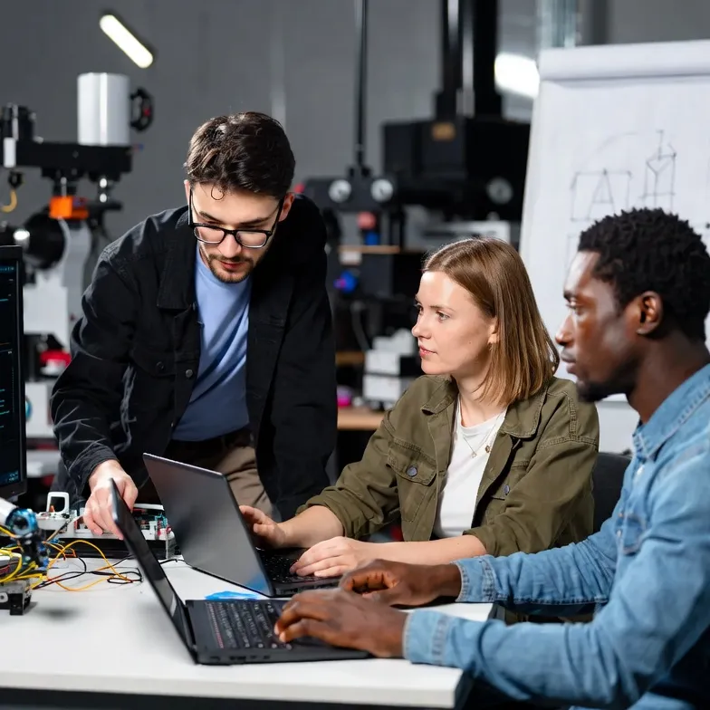 Ein Team arbeitet in einem Labor an der Entwicklung digitaler Technologien. Zu sehen sind Computer, Programmierumgebung und ein Roboterarm als Beispiele für moderne Automatisierungs- und KI-Anwendungen.