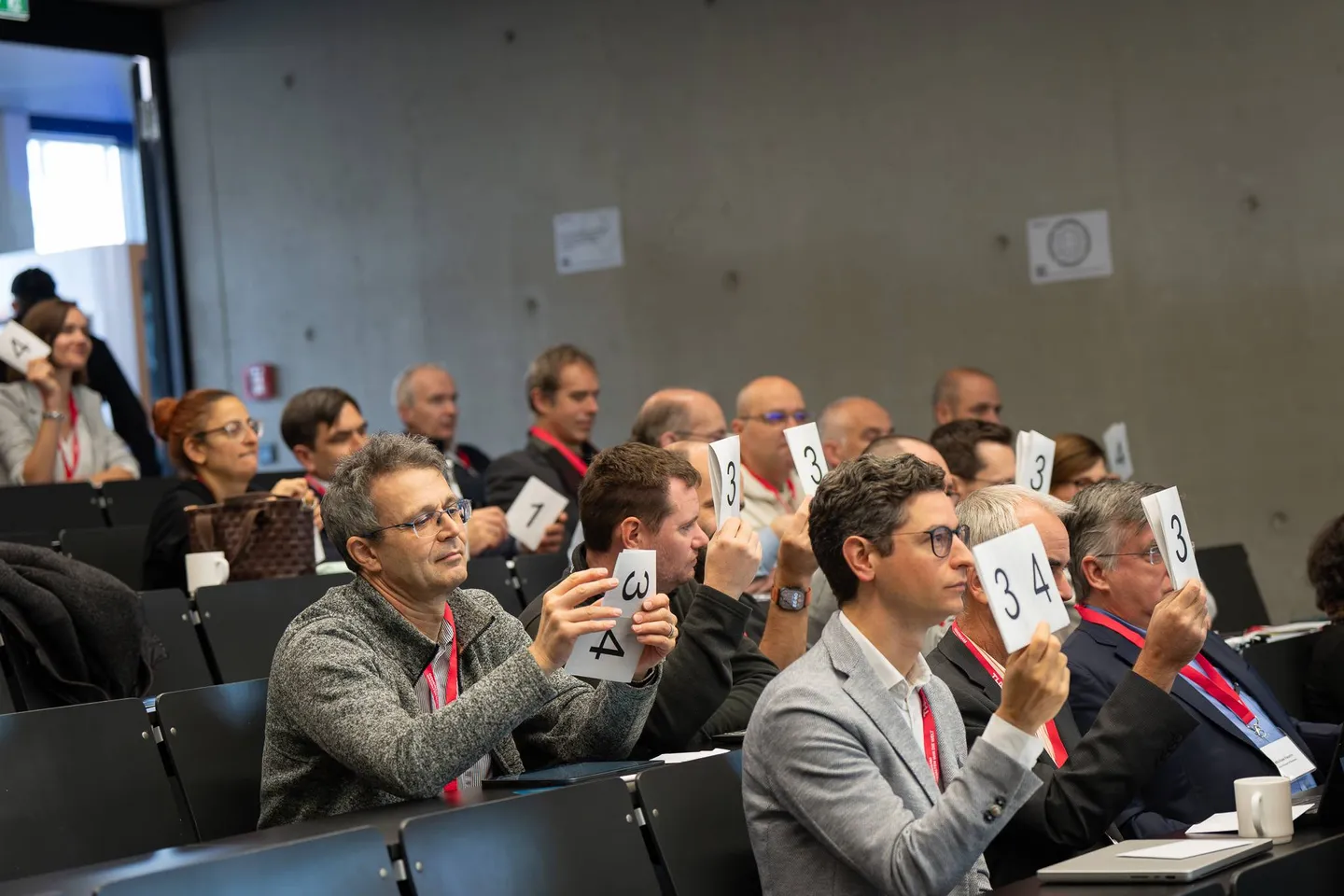 Teilnehmende im Hörsaal halten Abstimmungskarten hoch