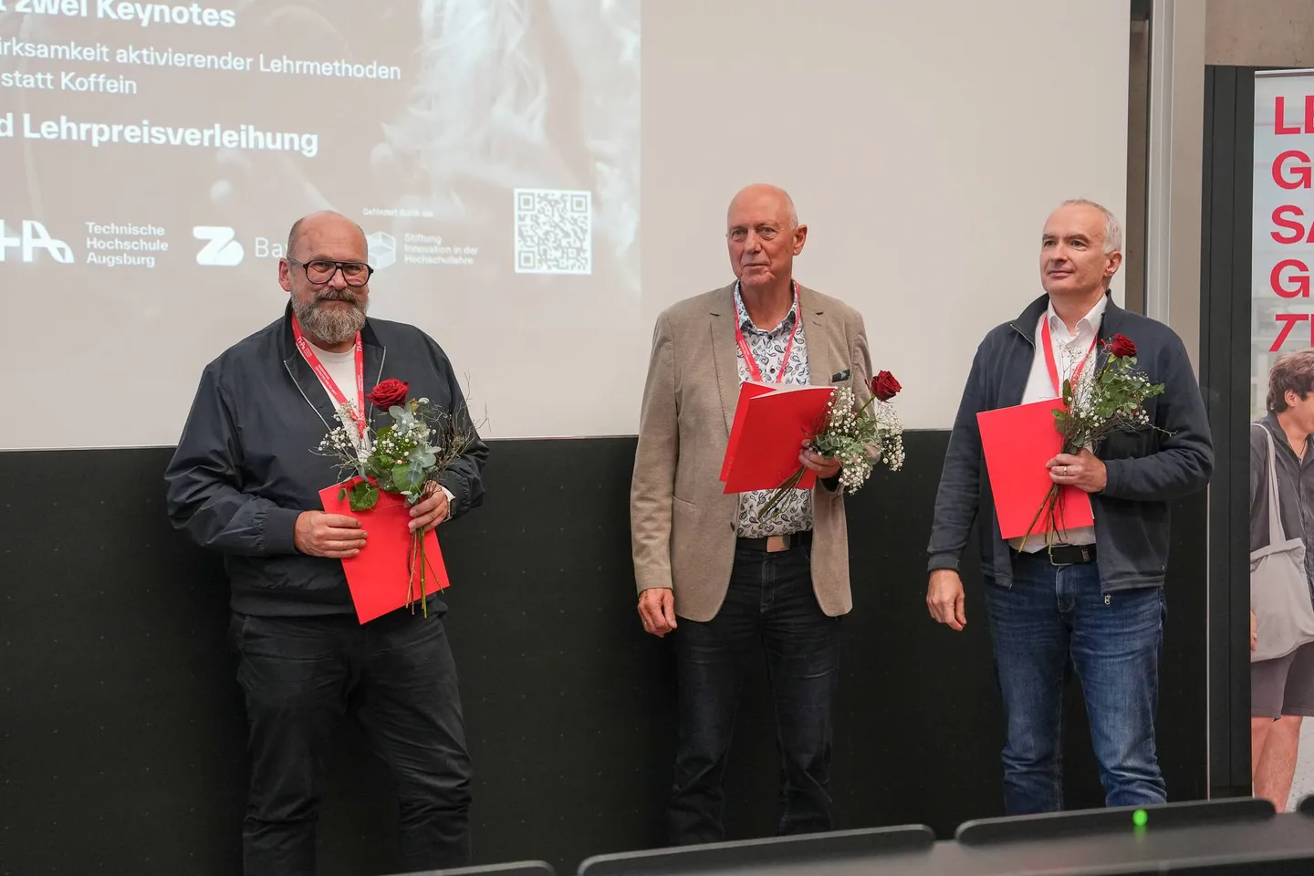 Drei Preisträger stehen mit Blumen und Urkunden nebeneinander