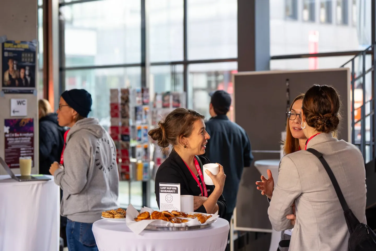 Teilnehmende stehen mit Kaffee an Stehtischen im Foyer