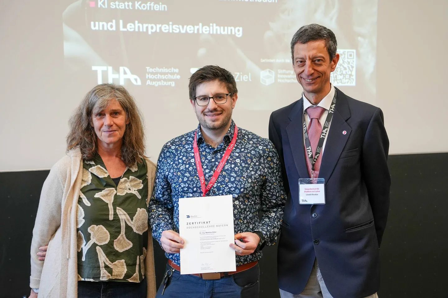 Drei Personen bei der Zertifikatsübergabe, der Ausgezeichnete hält die Urkunde in der Hand
