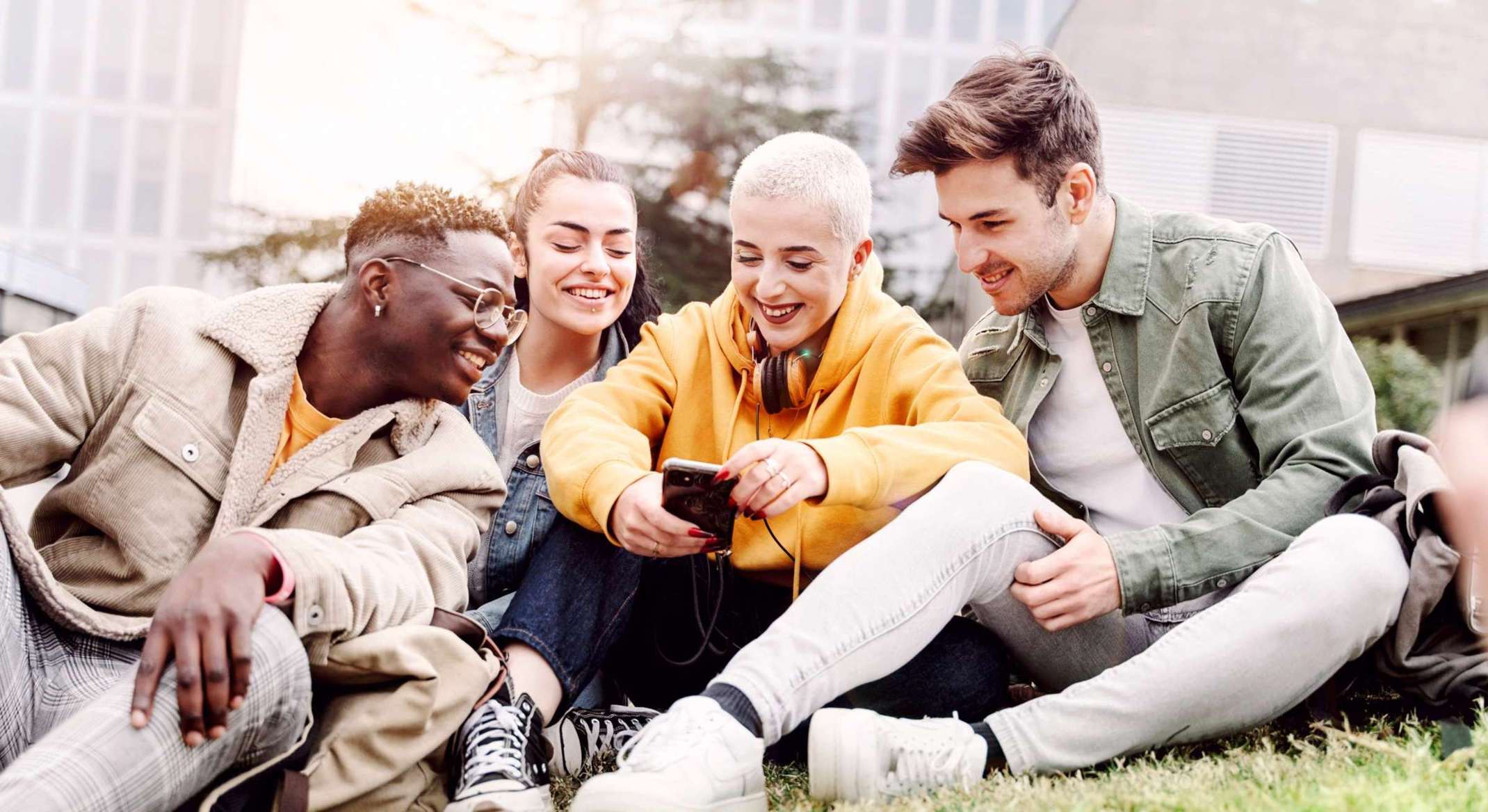 Jugendliche Frauen und Männer auf einer Wiese mit einem Handy in er Hand. Foto: adobestock