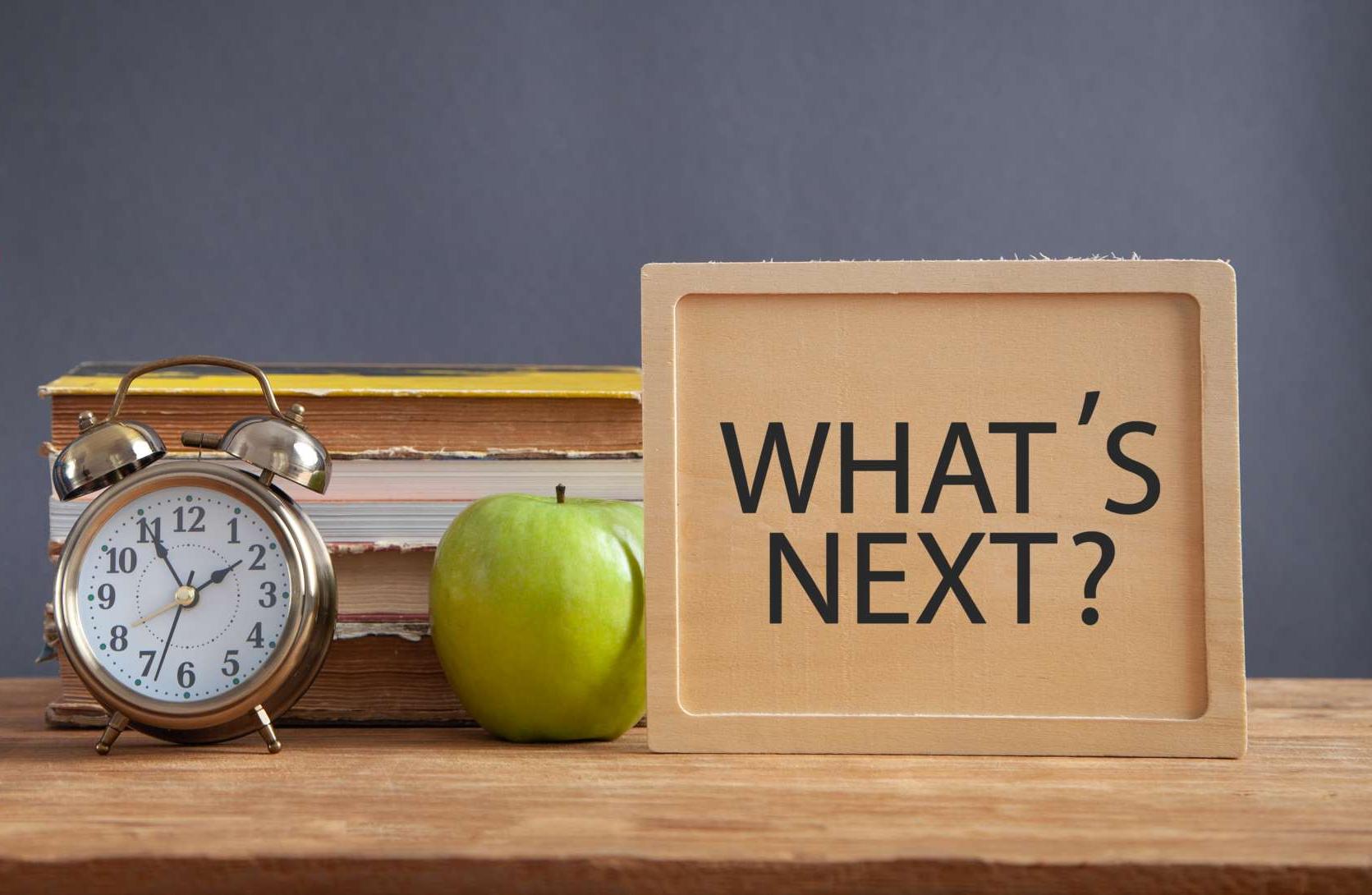 Tisch mit verschiedenen Schulutensilien darauf und der Frage "What's Next?" Tisch mit verschiedenen Schulutensilien darauf und der Frage "What's Next?"
