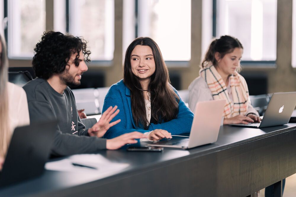Studierende unterhalten sich in der Vorlesung am Laptop
