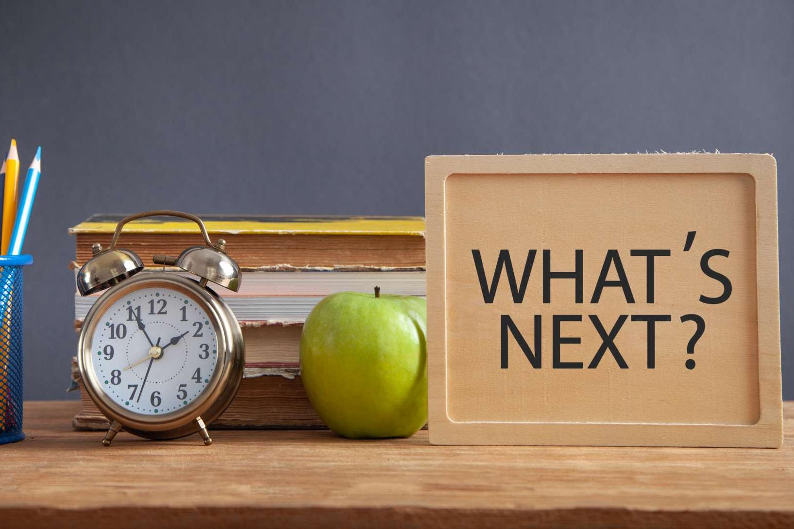 Tisch mit verschiedenen Schulutensilien darauf und der Frage "What's Next?"